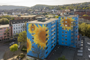  In Wuppertal blühen an der Hausfassade eines Hochhauses überdimensionale Sonnenblumen auf blauem Grund, komplettiert von ebenso großen Insekten 