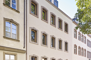  Neubau, der die Geschichte des Orts fortschreibt: Die Sandstein-Fensterfassungen des früheren Bestandsgebäudes wurden vor dem Abriss ausgebaut und in neuer Ordnung in die neue Fassade integriert. Ein feiner Filzputz und eine abgestimmte Farbigkeit korrespondieren perfekt mit den historischen Nachbarhäusern 