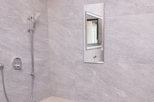  Clever durchdacht bis ins kleinste Detail: Eine Sitzmöglichkeit in der bodenebenen Dusche erleichtert die Pflege, der Duschablauf in der Wand sorgt hierbei für einen leichten Abfluss. Die Nischenablagebox mit Einlegeböden und verspiegelter Schiebetür wurde direkt platzsparend in die Ziegelwand installiert 