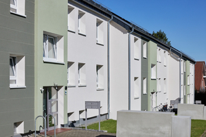  Die verputzte Fassade ist in cremefarbene, grau- sowie pistaziengrüne Bereiche gegliedert. So liegt der Fokus klar auf den Eingangsbereichen des versetzt angeordneten Gebäudes 