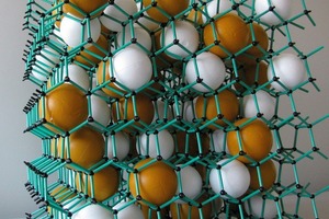  Modell des Nano-Quarz-Gitters, in dem anorganisches Nano-Silica (schwarz, 25 nm) mit organischen Acrylatpolymeren (grünes Gitter) fest miteinander verbunden sind. Das Titandioxid (weiß, Durchmesser 250 nm) und die Pigmente (ocker, Durchmesser 300 nm) sind fest in die NQG-Struktur eingebunden 