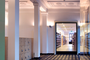  Die Eingangshalle mit ihrer stuckverzierten Decke, den Bodenfliesen und halbrunden Nischen wurde originalgetreu rekonstruiert, das große Glasfenster erlaubt den Blick in die moderne Bibliothekslandschaft 